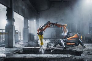En orange rivningsrobot utför precisionsarbete i en dammig industrimiljö.