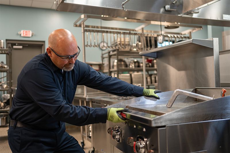 Tekniker utför service på en stekhäll i ett professionellt storkök.