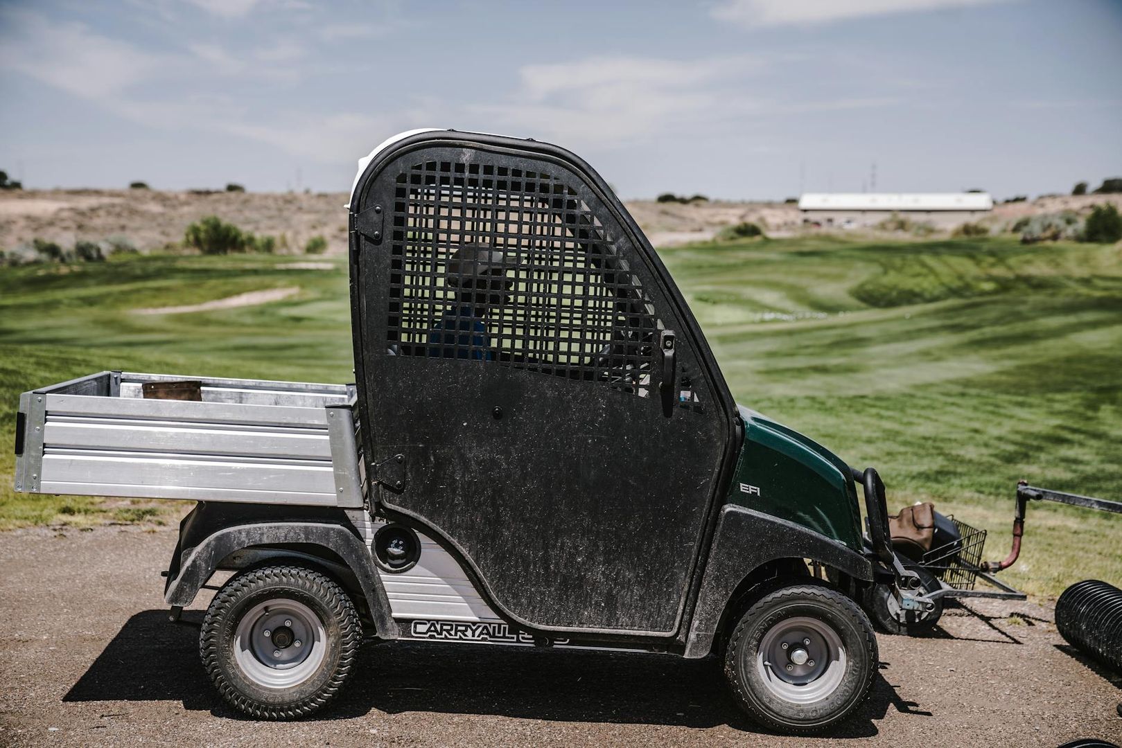 Ett grönt arbetsfordon av modellen Carryall parkerat vid en golfbana.